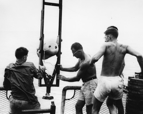 Robert Floyd Dill, Walter Heinrich Munk, and Richard Blumberg prepare to lower a deep-sea camera enclosed in a watertight case into the ocean