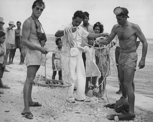 Henri Rotschi (left) holds a basket used to collect pearl shell, while Tehaiere Paniora (center) and Willard N. Bascom (right) examine weight line
