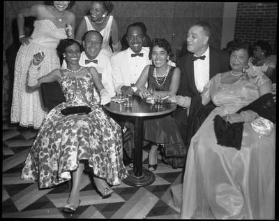 Royal Towns (back left) seated with group of men and women in evening attire in nightclub