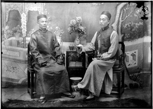 Portrait of two Chinese men, seated, holding incense and pipes