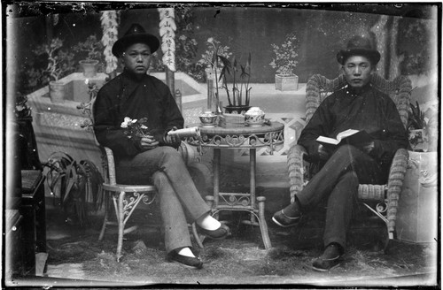 Portrait of two Chinese men seated on either side of a small table