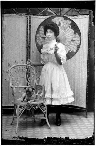 Portrait of a Chinese woman standing and holding parasol, with a small dog on a chair