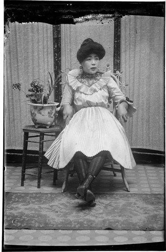 Portrait of a Chinese woman seated, wearing pleated dress and striped stockings
