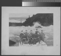 Group portrait, nine men in coats and hats, imposed on image of river rapids, 1890 [recto]