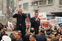 President Johnson covers his ears during a campaign parade in California