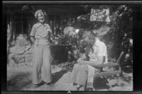 Mertie West poses while Nina Meyers watches Glen Velzy mend the back of his chair, San Gabriel Mountains, 1941