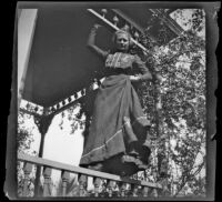 Worm's-eye view of Louise Ambrose posing while standing atop a porch rail, Los Angeles, about 1894