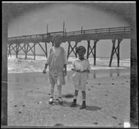 Frances West and Chester Schmitz stand on the beach with a pier in the background, Venice, about 1915