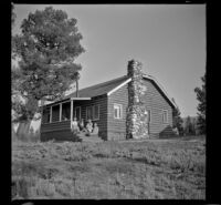 Distant view of Wayne West, Mertie West, Maud West, Agnes Whitaker and Forrest Whitaker sitting on the front porch of their cabin, Big Bear Lake, 1945