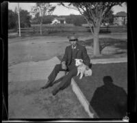 Wilson West sits on a curb with a dog, Los Angeles, 1898