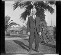 Abraham Whitaker stands in Alhambra Park in front of a large palm tree, Alhambra, about 1930