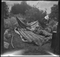 H. H. West Jr. lying on a bed during a camping trip, Inyo County vicinity, about 1930