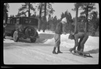 Neil Wells hitches a sled to H. H. West's Buick as Mertie West watches him, Big Bear, 1932