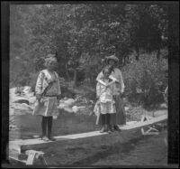 Frances West, Elizabeth West and Mary A. West standing on a wood plank over a stream, San Francisquito Canyon, about 1915
