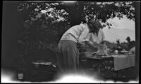 Agnes Whitaker and Mertie West prepare food at a table in a campsite, Inyo County vicinity, about 1930