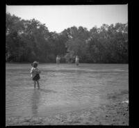 Elizabeth West stands in the water while her mother, Mary West and Bessie Velzy stand in the background, Anaheim vicinity?, 1909