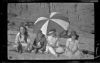 Elizabeth West, Chester Schmitz, Frances West and Irene Schmitz sit in front of a beach umbrella, Santa Monica, [about 1915]