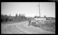 H. H. West poses beside signs advertising Santa Claus Lodge and Coca-Cola, Gulkana, 1946