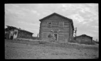 Two people stand outside the log buildings, Circle, 1946