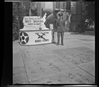 Lynn West poses by the handprints at Grauman's Chinese Theatre next to a display for war bonds, Los Angeles, 1942