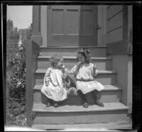 Frances and Elizabeth West sit on the back steps of a house with a teddy bear between them, Los Angeles, about 1907