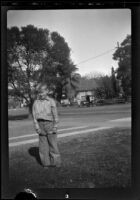 Boy stands on the front lawn of the West's house holding a feather, Los Angeles, about 1930