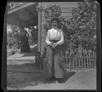 Mertie Whitaker stands at the side of a house, while and Ellen Lorene (Pinkie) Lemberger stands on the porch, Crafton, 1901