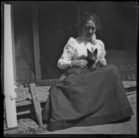 Frances Nichols holds a cat in her lap while sitting on the front porch, Santa Ana, about 1899