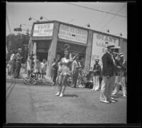 Drum majorette, members of a marching band, and spectators stand in front of Van's Malt Shop, Glendale, 1937