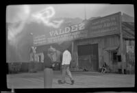 Mertie stands on a dock and fiddles with a camera, Valdez, 1946