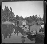 People walk across on stepping stones to cross the lake at Lincoln (Eastlake) Park, Los Angeles, about 1900