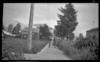 Mertie West walks with the Presbyterian minister's wife past the school, Metlakatla, 1946