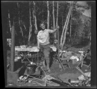 Agnes Whitaker holds a shovel while H. H. West Jr. sits at a table behind her at Convict Lake, Mammoth Lakes vicinity, 1929