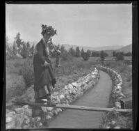 Ellen Lorene (Pinkie) Lemberger walks a wood plank over a stream while holding a dead rabbit, Crafton, 1901