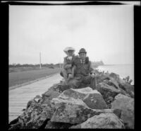 H. H. West and his wife, Mary, sit on the rocks with the Hotel del Coronado in the distance, Coronado, 1909