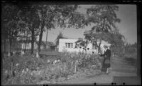 Mertie West stands by a flower garden, Anchorage, 1946