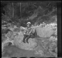 Frances West sits atop a small boulder in a stream, Sunland-Tujunga vicinity, 1912