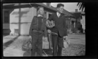 H. H. West Jr. and another boy stand on the West's driveway holding luggage and packages, Los Angeles, about 1930