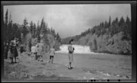 Mertie West stands on a riverbank in front of Bow Falls, Banff, 1947