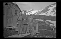 Three servicemen stand on the wood slat walkway outside the barracks, Dutch Harbor, 1943