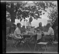 Mertie West stands at a table as Agnes Whitaker, Forrest Whitaker, and William Shaw eat breakfast at a campsite, Inyo County vicinity, about 1930