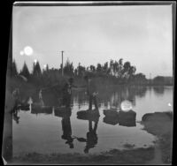 Men helps a woman across the stepping stones at Lincoln (Eastlake) Park as a boy follows behind, Los Angeles, about 1900