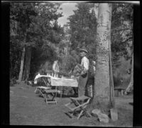 Abraham Whitaker stands by a tree while Edith Shaw, Mertie West and Agnes Whitaker stand by a table at their campsite, Modoc County, 1929