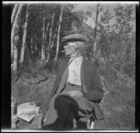 Abraham Whitaker smokes a cigar and sits on a chair while camping at Convict Lake, Mammoth Lakes vicinity, 1929