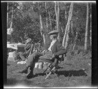 Abraham Whitaker sits on a chair while H. H. West Jr. sits at a table while camping at Convict Lake, Mammoth Lakes vicinity, 1929