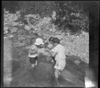 Frances Cline, Frances West and Elizabeth West wade in Big Tujunga Creek as they peer at something held in a cloth, Sunland-Tujunga vicinity, 1912