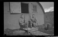 Two servicemen crouch in front of the barracks and pose with their guns, Dutch Harbor, 1943