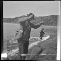 Glen Velzy climbs up the rocks carrying both a fish he caught and his fishing rod, Laguna Beach, 1914