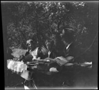 Mertie West, H. H. West, Jr. and H. H. West, Sr. sit at a table under the oaks at Soper's Ranch, Ojai vicinity, about 1927