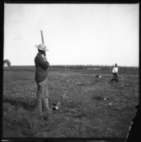 William Mead stands with a gun while another man runs away from the trap, which has been set to fling a clay blackbird, Elliott vicinity, 1900
